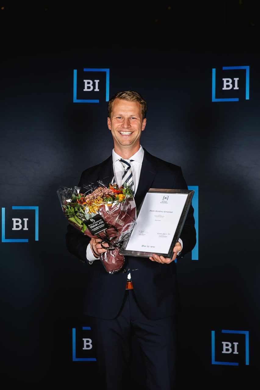 Mads Nordmo Arnestad smilende med blomster og en innrammet undervisningspris foran BI-logoer